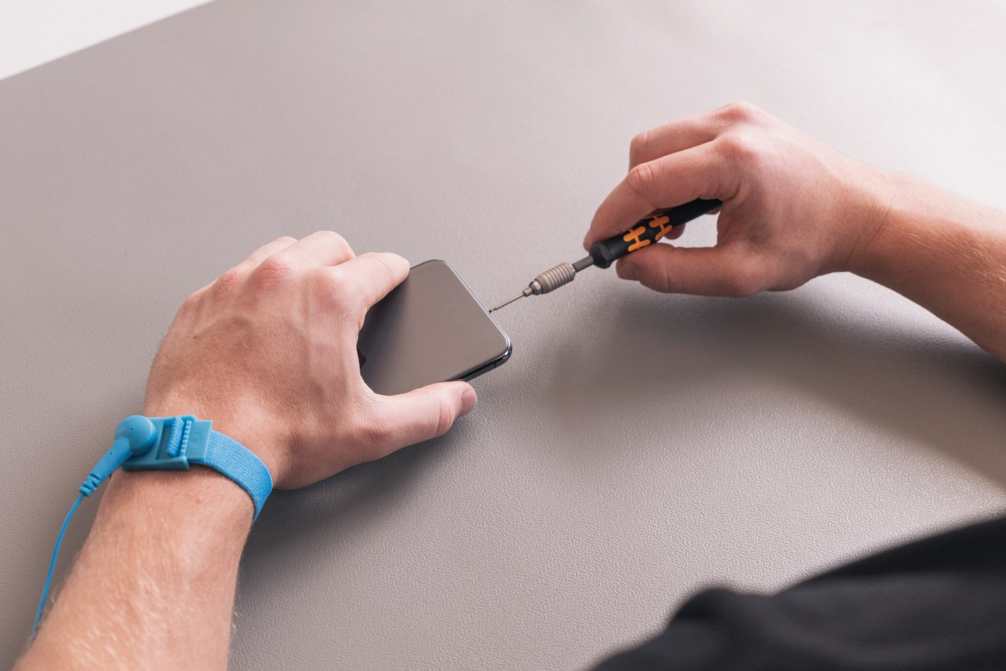 Manos reparando un smartphone gris oscuro con un destornillador.