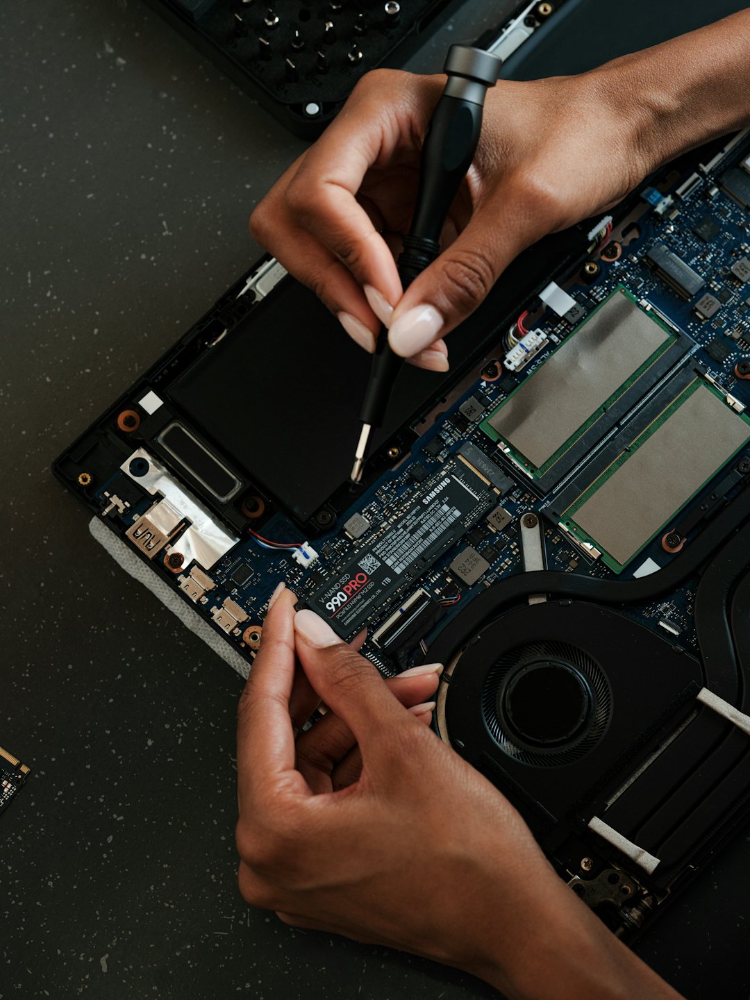 Manos reparando un portátil con destornillador y SSD.